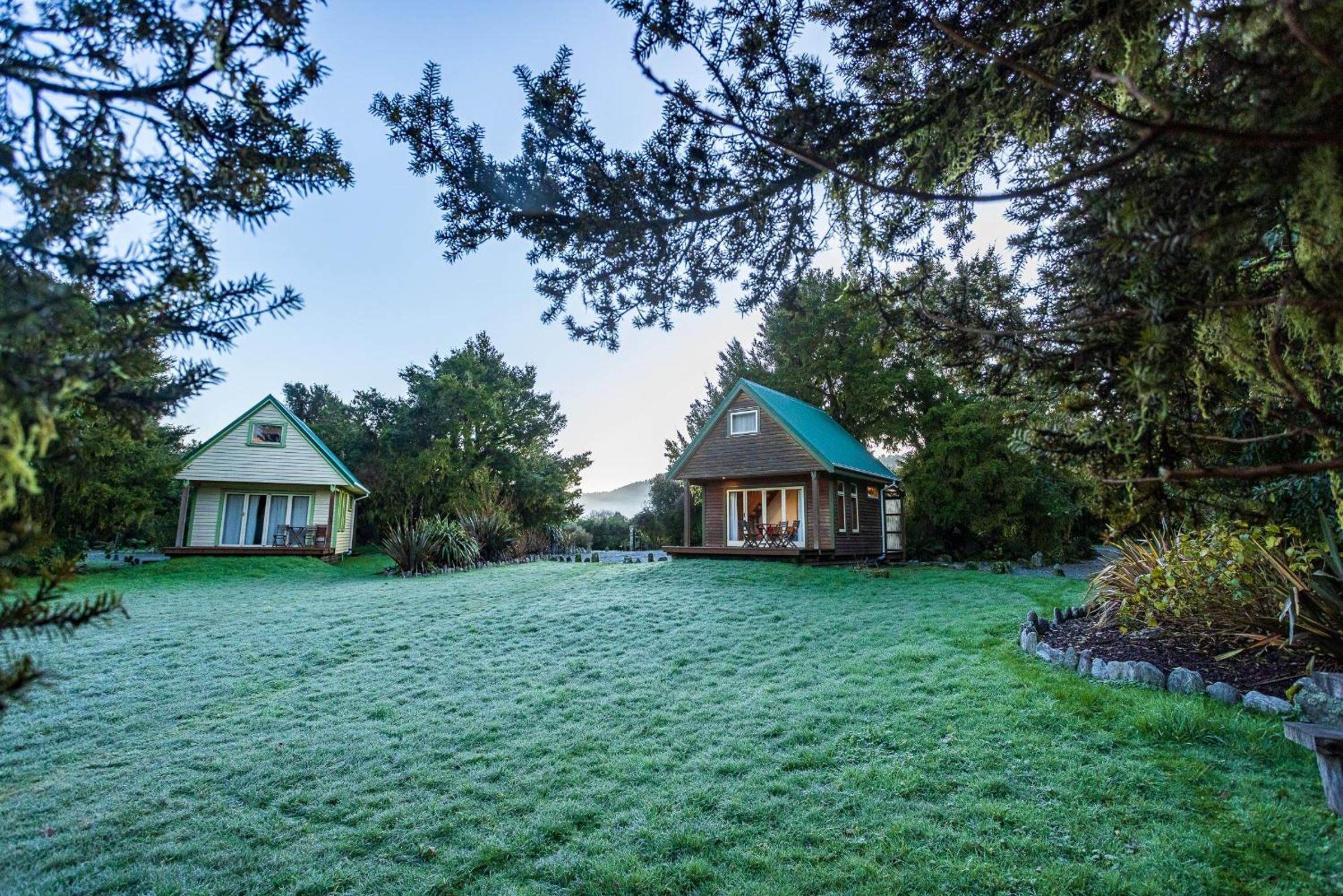Two houses with green roofs, surrounded by a grassy yard and trees.