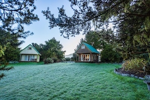 Duas casas com telhados verdes, cercadas por um gramado e árvores.