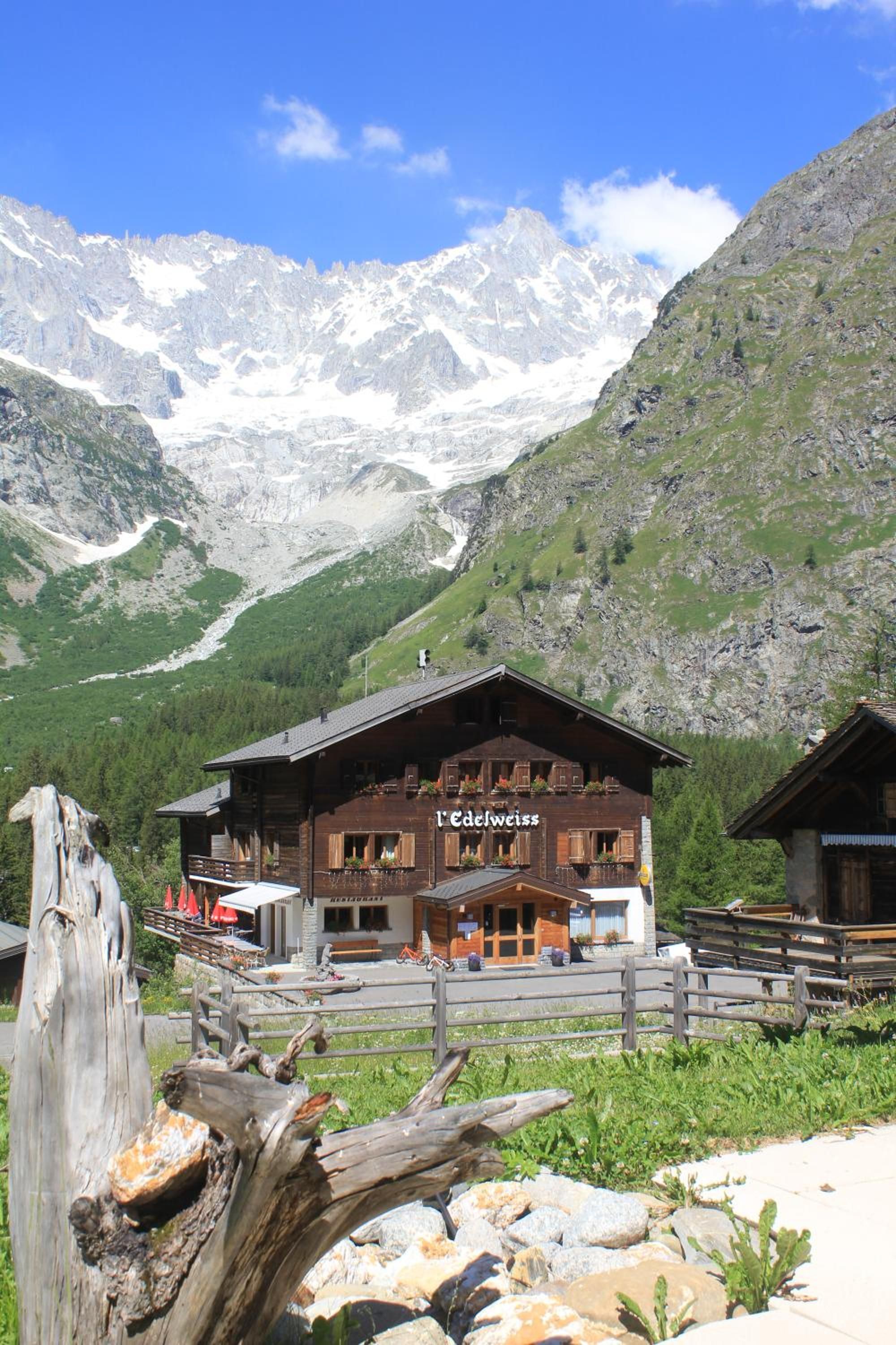 Un albergue de montaña con fachada de madera, un letrero de restaurante y vistas a montañas nevadas.