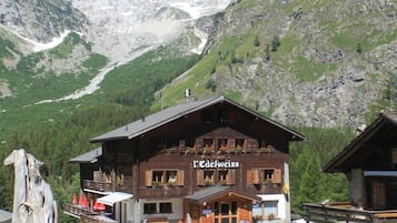 A mountain lodge with a wooden facade, a restaurant sign, and a view of snow-capped mountains.