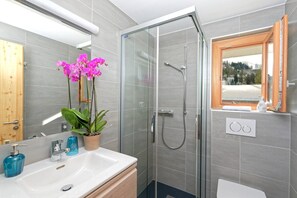 Un baño con cabina de ducha de vidrio, un lavabo con espejo y una ventana con vistas al exterior.