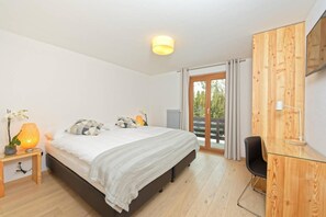 Un dormitorio con cama, escritorio, silla, lámpara y vista al exterior.