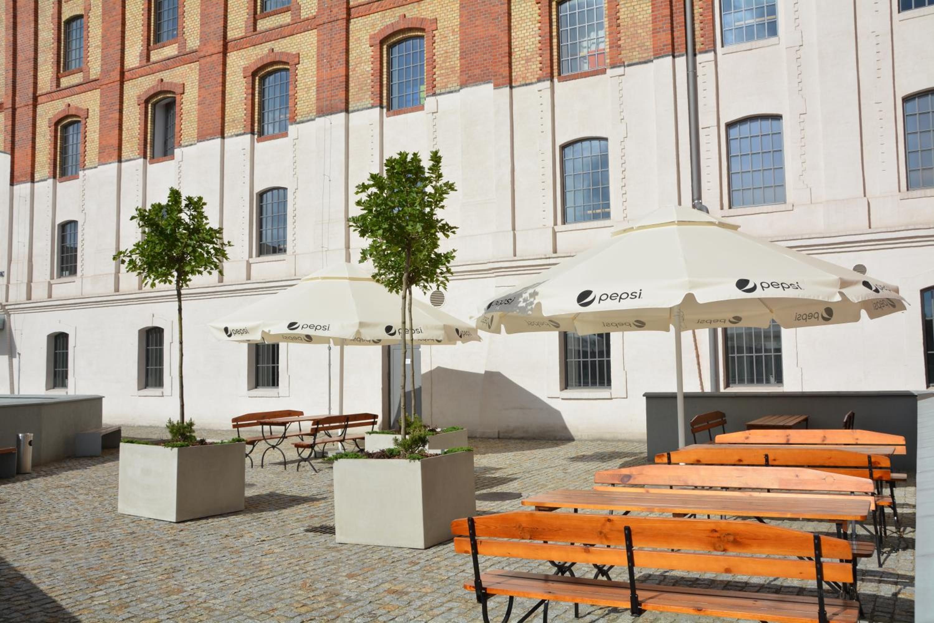 An outdoor seating area with tables and benches, umbrellas, and potted plants.