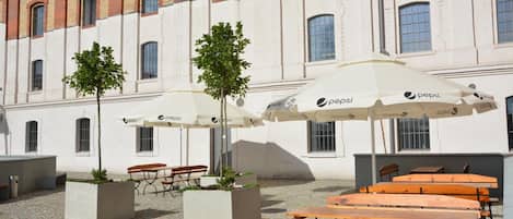 An outdoor seating area with tables and benches, umbrellas, and potted plants.