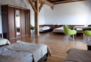A room with wooden flooring, a wardrobe, two beds, a desk, and two green chairs. - Hostel Mi Odzynarodowe Centrum Spotka N M Codzie Y (Torun)