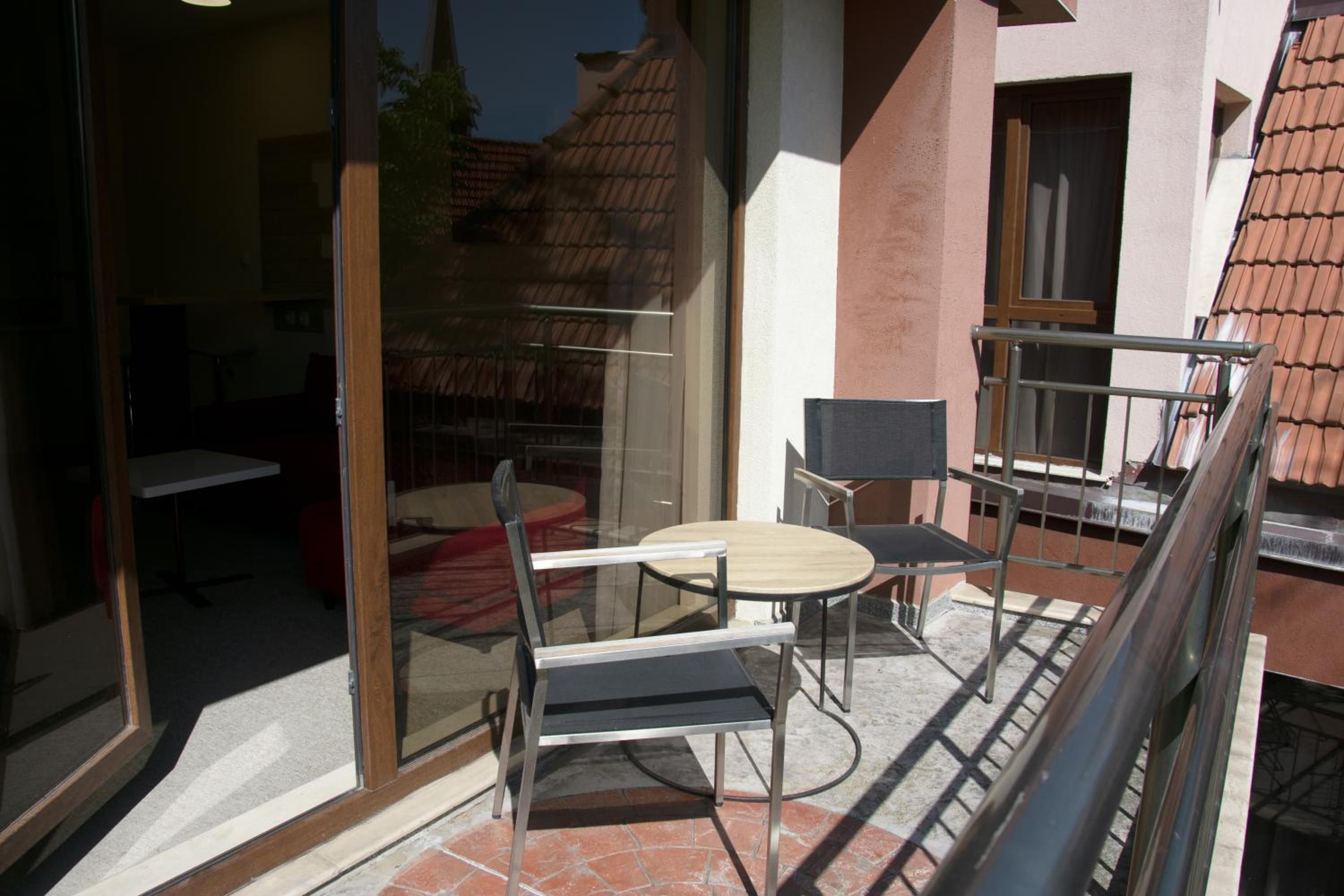 A glass door leading to a patio with a round table and chairs, a small table, and a window overlooking a building with a tiled roof.