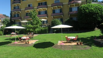 Un patio con mesas al aire libre y sombrillas, rodeado por un edificio de varios pisos con balcones.