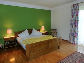 A bedroom with a wooden bed, green walls, two bedside lamps, a floral curtain, and a wooden floor.