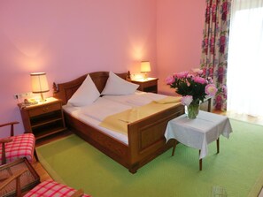 A neatly made bed with white linens, two bedside lamps, a floral vase on a small table, and a checkered chair. - Hotel Posthof (Millstatt)