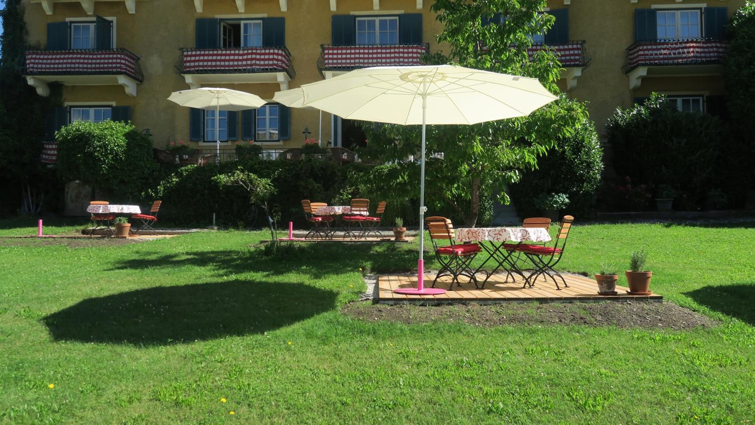 Een terras met tafels en stoelen, parasols en een gebouw op de achtergrond.
