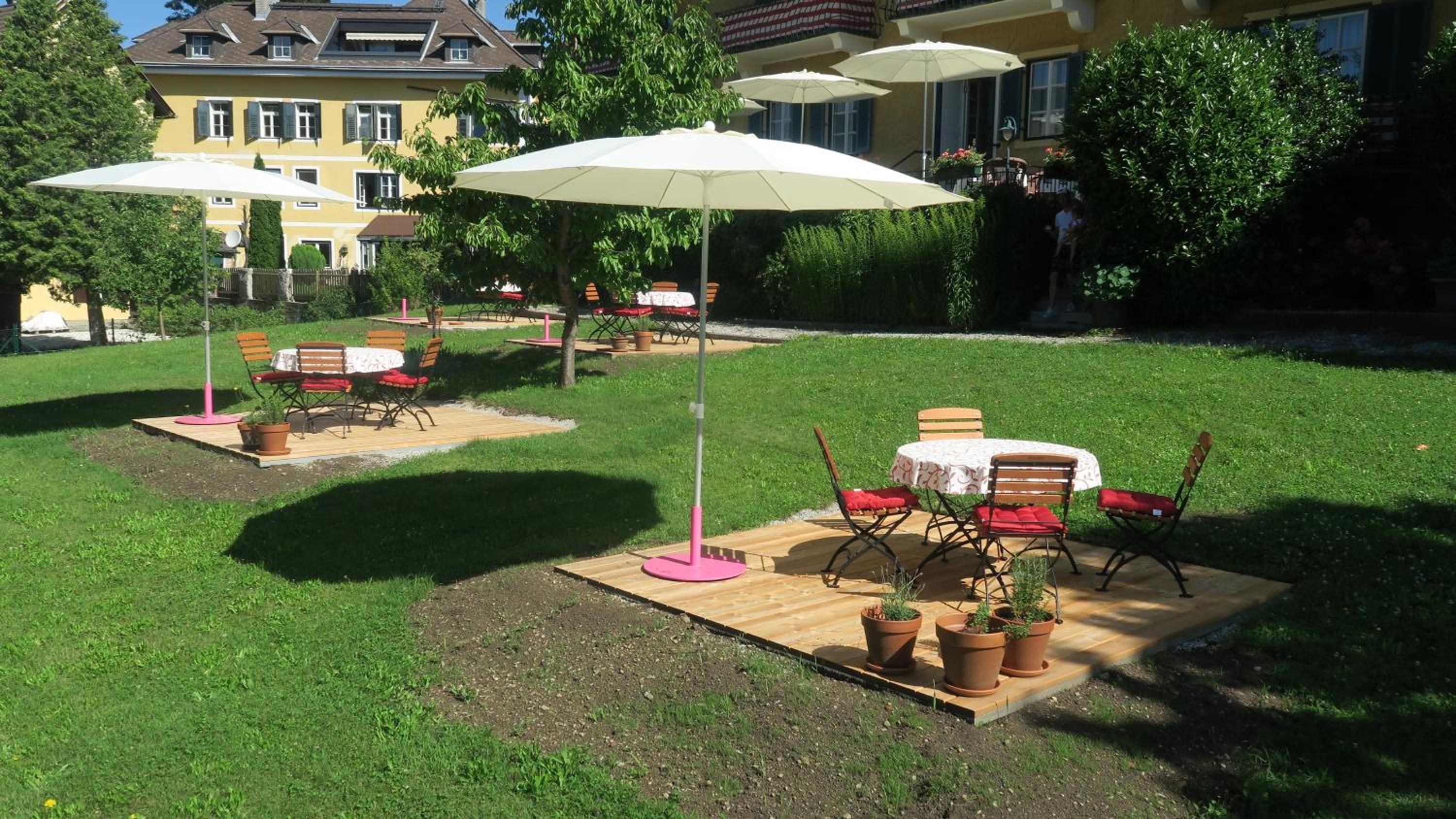 An outdoor patio area with tables and chairs, surrounded by potted plants and umbrellas.