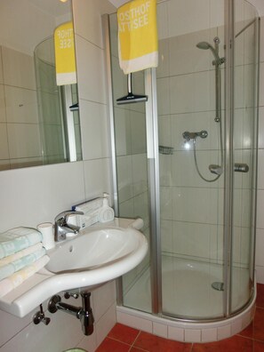 A bathroom with a glass-enclosed shower, a sink with a mirror, and a towel rack. - Hotel Posthof (Millstatt)