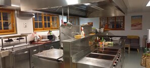 A commercial kitchen with stainless steel appliances, a large stove, and various cooking utensils. - Freeride Hostel Bar (Val d'Illiez)