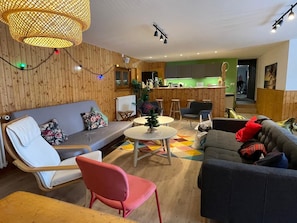 Ett modernt vardagsrum med en soffa, stolar, ett litet bord och ett köksområde i bakgrunden.