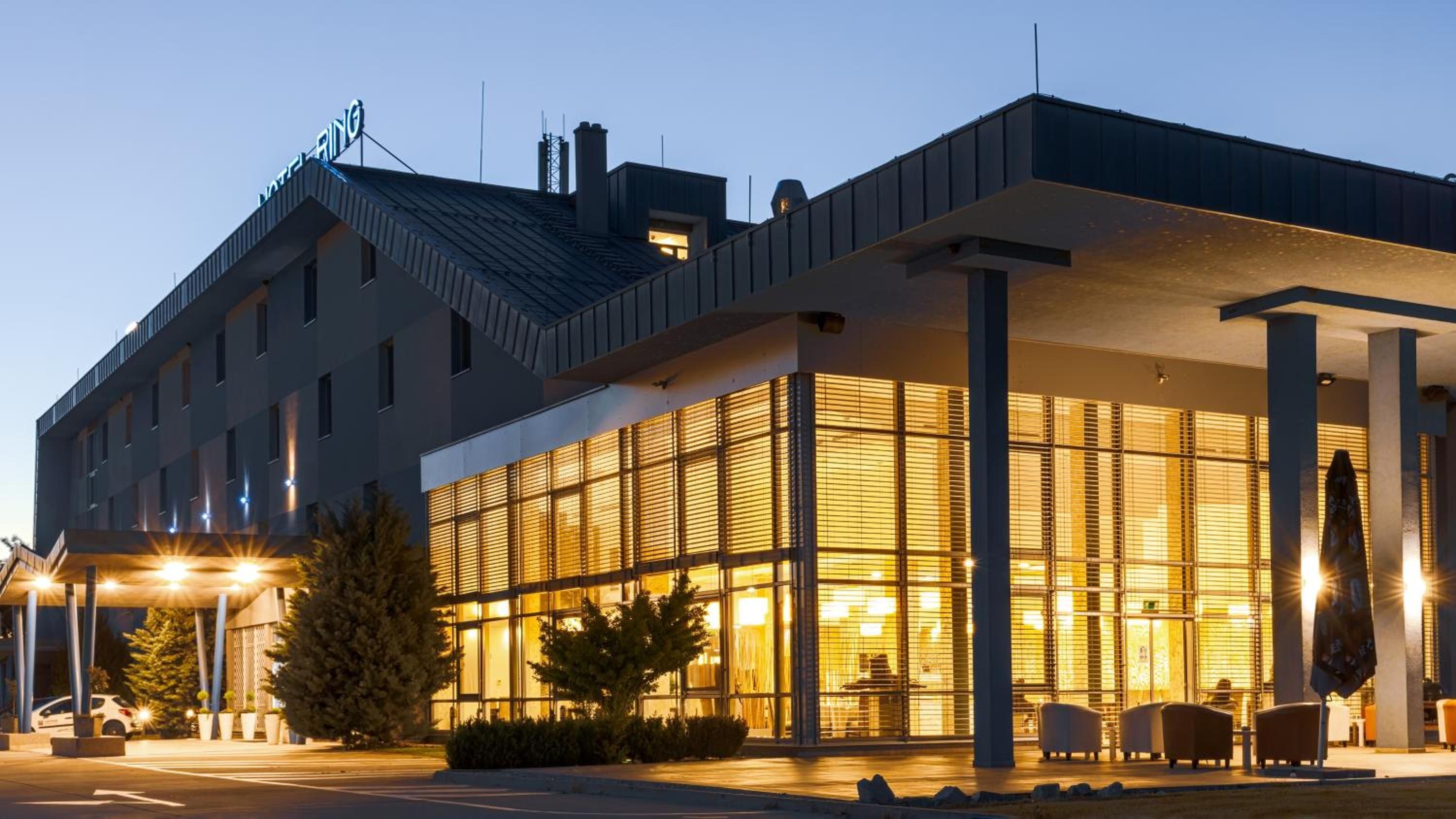 A modern hotel with a glass facade, outdoor seating, and a covered entrance.