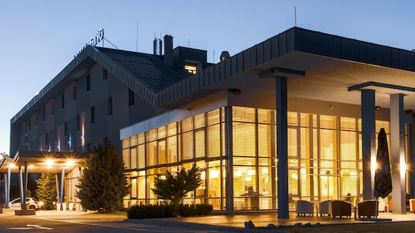A modern hotel with a glass facade, outdoor seating, and a covered entrance.
