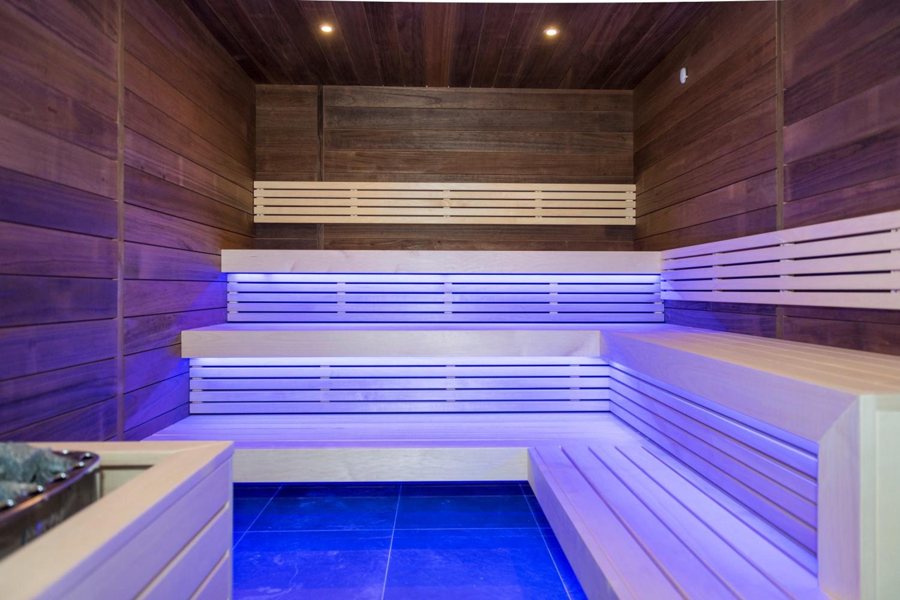 A sauna with wooden walls and benches, a tiled floor, and a ceiling with recessed lighting.