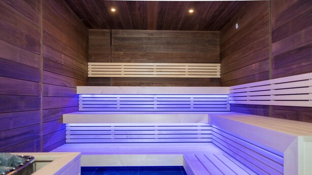 Uma sauna com paredes e bancos de madeira, piso ladrilhado e teto com iluminação embutida.
