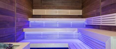 A sauna with wooden walls and benches, a tiled floor, and a ceiling with recessed lighting.
