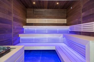 Una sauna con paredes y bancos de madera, suelo de baldosas e iluminación empotrada en el techo.
