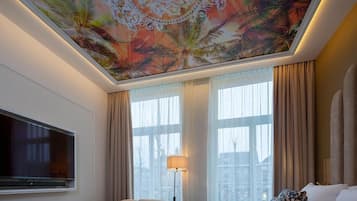 A hotel room with a large bed, a flat-screen TV, a sofa, and a ceiling with a floral pattern.