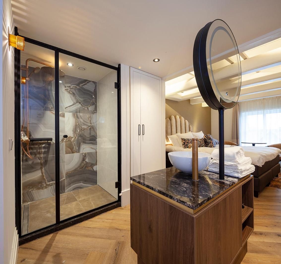 A modern hotel room with a glass-enclosed shower, a wooden vanity with a marble countertop, and a large mirror.