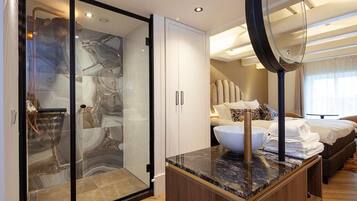 A modern hotel room with a glass-enclosed shower, a wooden vanity with a marble countertop, and a large mirror.