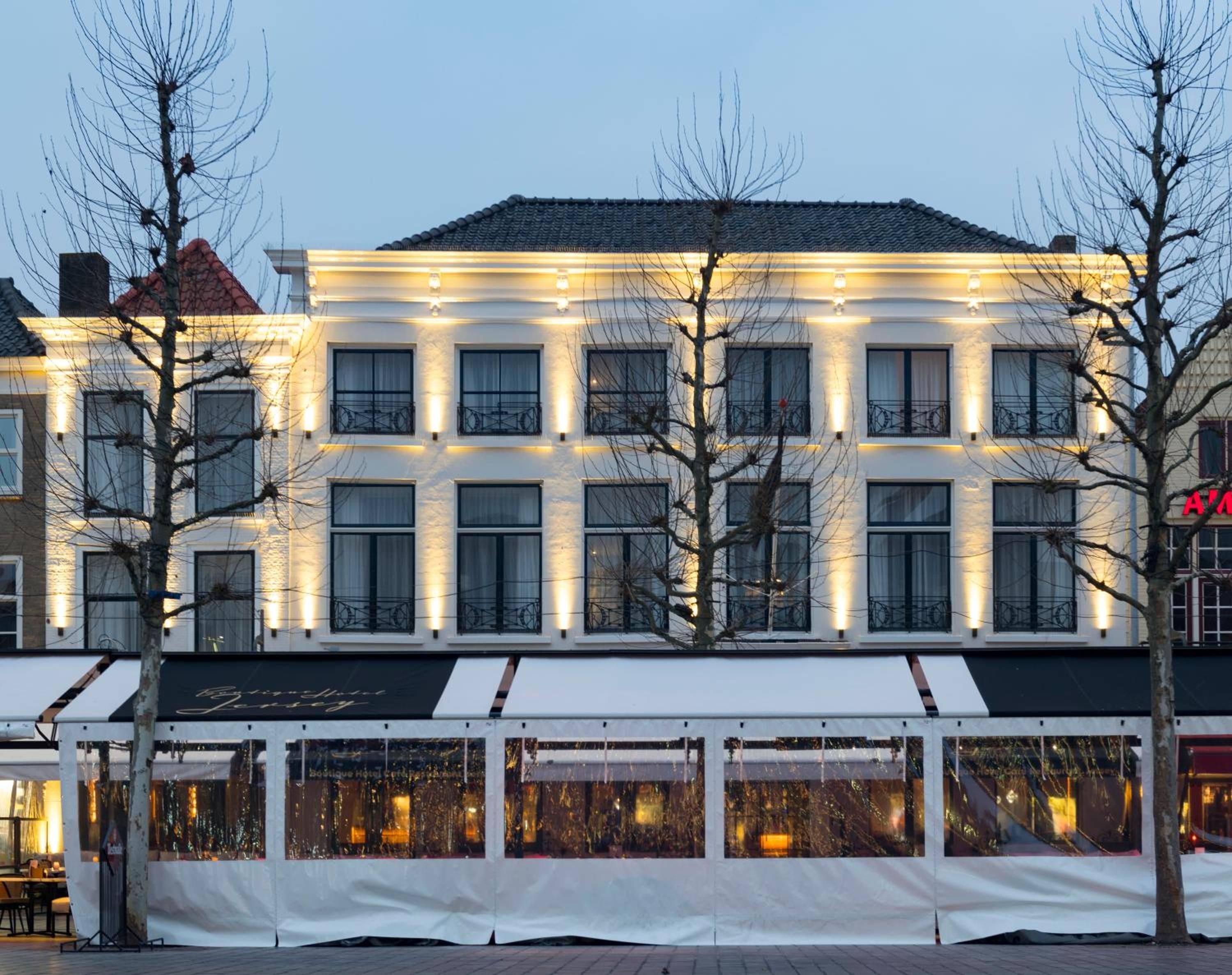 A hotel with a white facade, multiple windows, and a covered outdoor seating area.