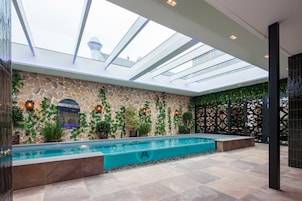 Un área de piscina interior moderna con tragaluces, paredes de piedra y plantas en macetas.