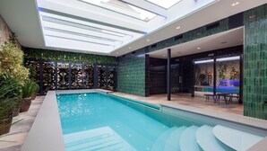 Uma área interna de piscina moderna com teto skylight, piscina com degraus de acesso e porta de vidro que dá para área externa.