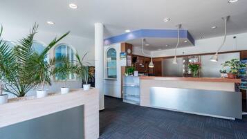Un área de recepción con mostrador, plantas en macetas, un reloj y una pared azul decorativa.