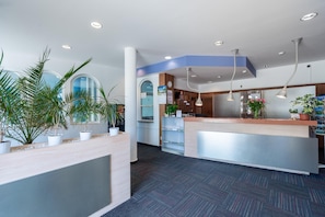 A reception area with a reception desk, potted plants, a clock, and a blue accent wall. - Hotel Floret (Pruhonice)