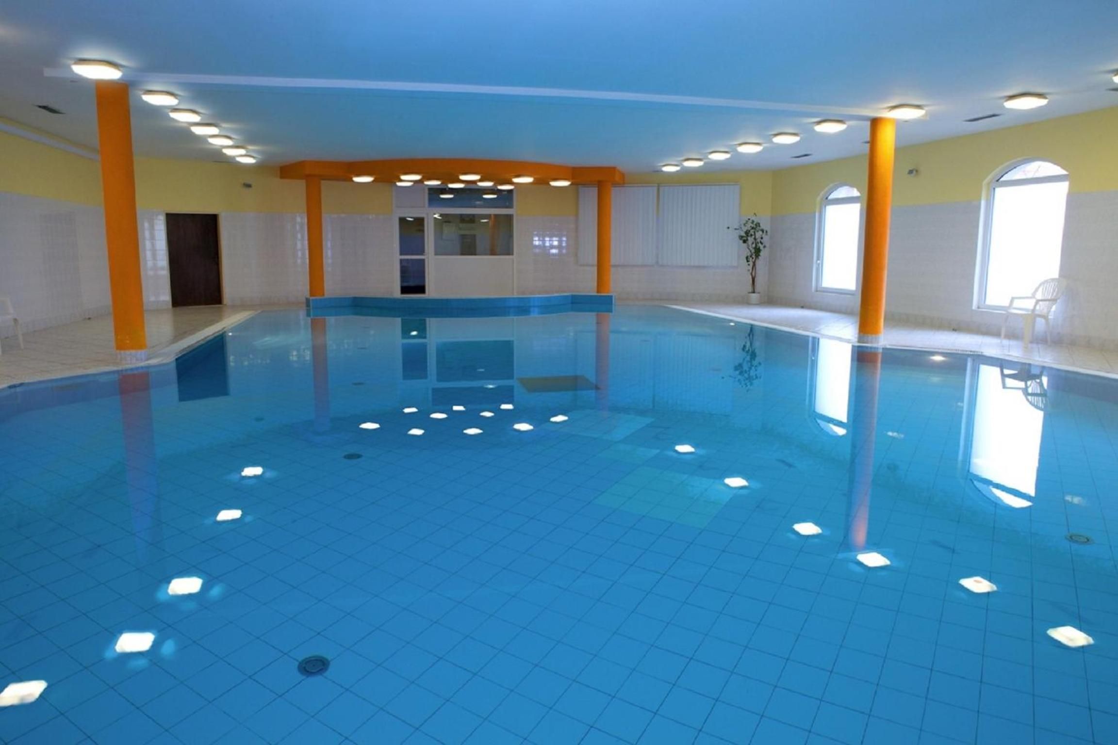 Ein Innenpool mit gefliestem Boden, umgeben von Wänden mit Fenstern und Türen.