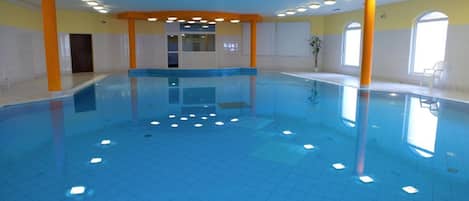 An indoor swimming pool with a tiled floor, surrounded by walls with windows and doors.
