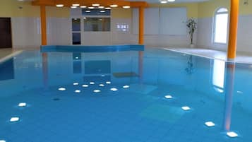 Una piscina interior con suelo de baldosas, una zona central de natación y una puerta que da a otra habitación.