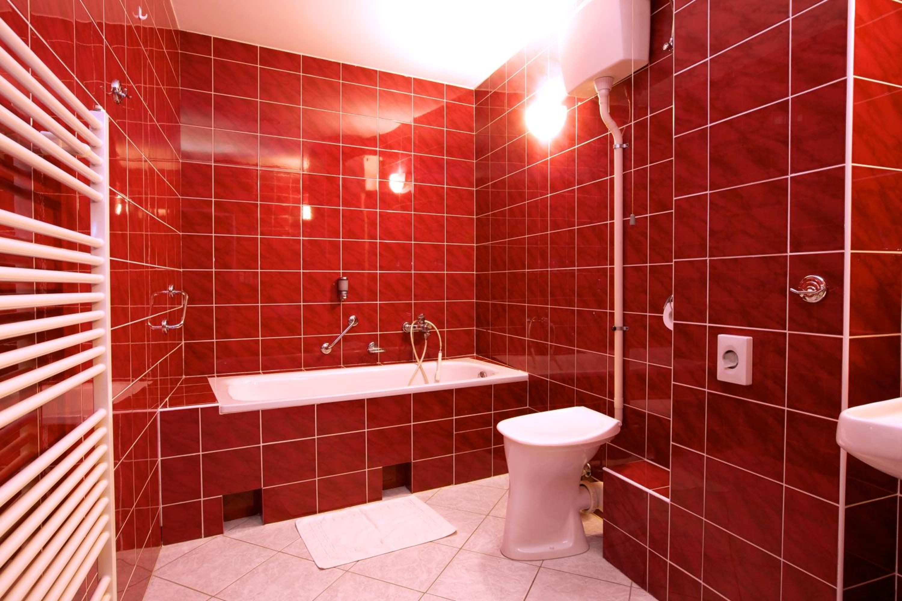 Ein Badezimmer mit roten Fliesen, einer weißen Badewanne, einer weißen Toilette und einem weißen Waschbecken.