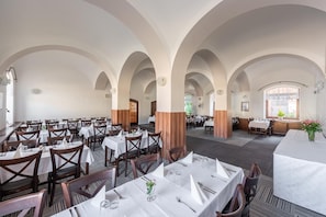A restaurant with multiple tables, wooden chairs, and white tablecloths. - Hotel Floret (Pruhonice)