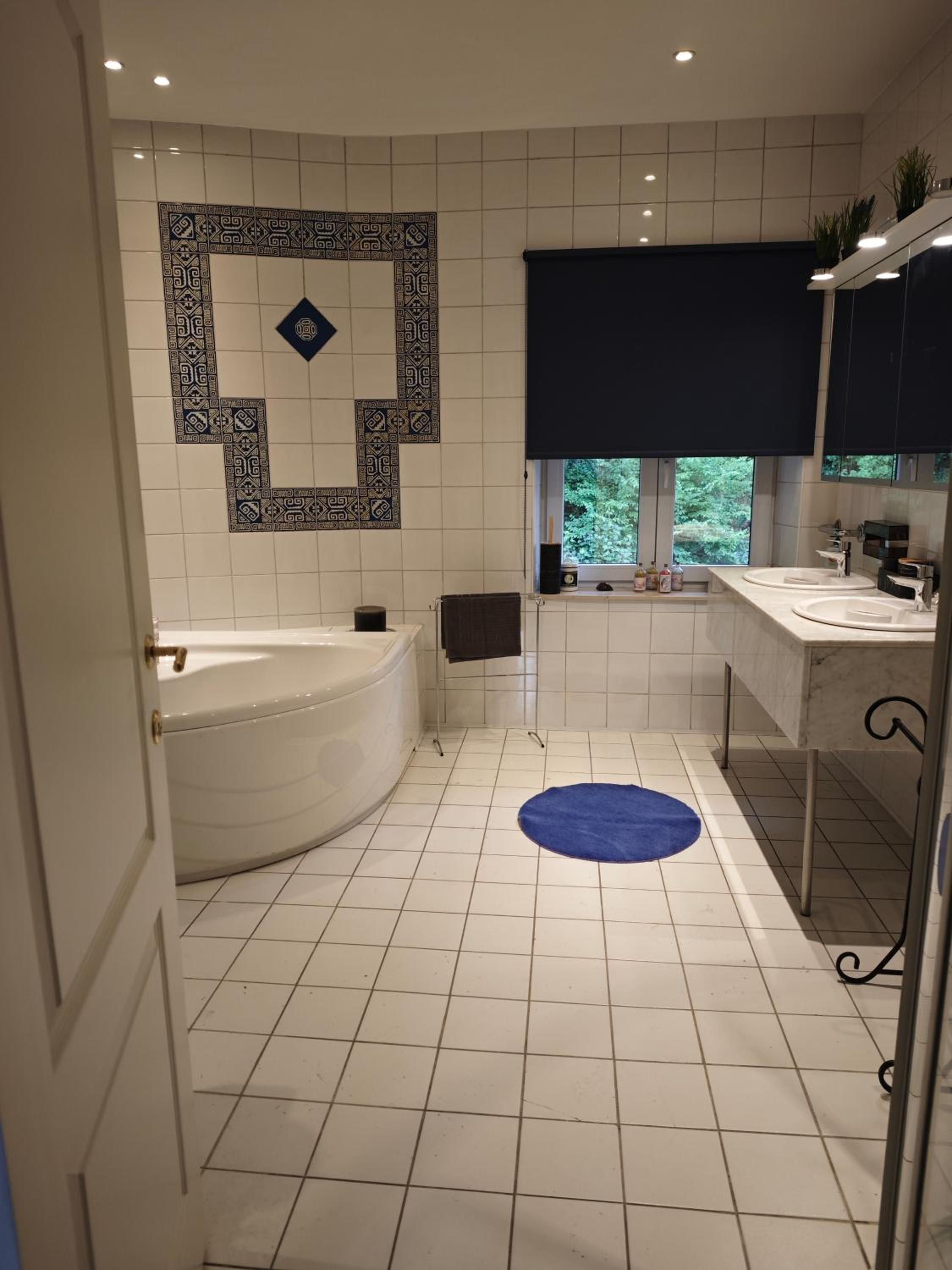 A bathroom with a bathtub, a sink, a window, and a patterned wall.