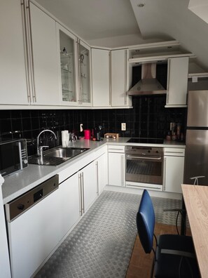 A modern kitchen with white cabinets, a stainless steel sink, and a built-in oven. - Stone Station (Esneux)