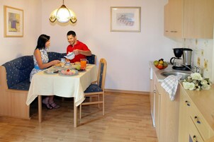 A dining area with a table set for two, a kitchen with a coffee maker, and a sofa.