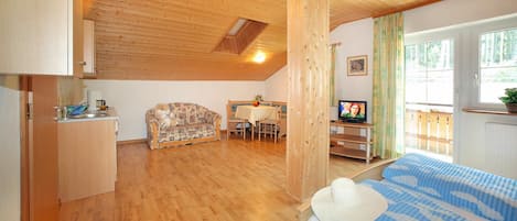 A cozy room with a bed, a sofa, a dining table, and a TV.