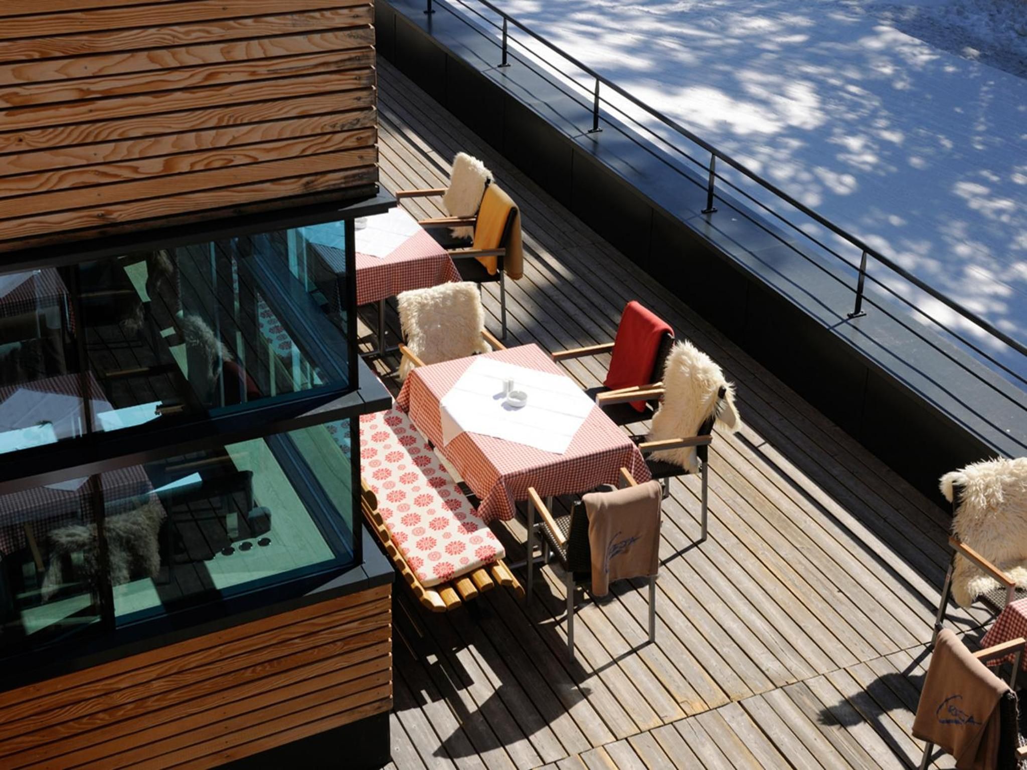 A deck with outdoor seating, including tables and chairs, and a glass enclosure with a view of the interior.