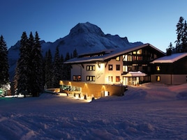 A multi-story hotel with a ski slope in the foreground and a mountain in the background.