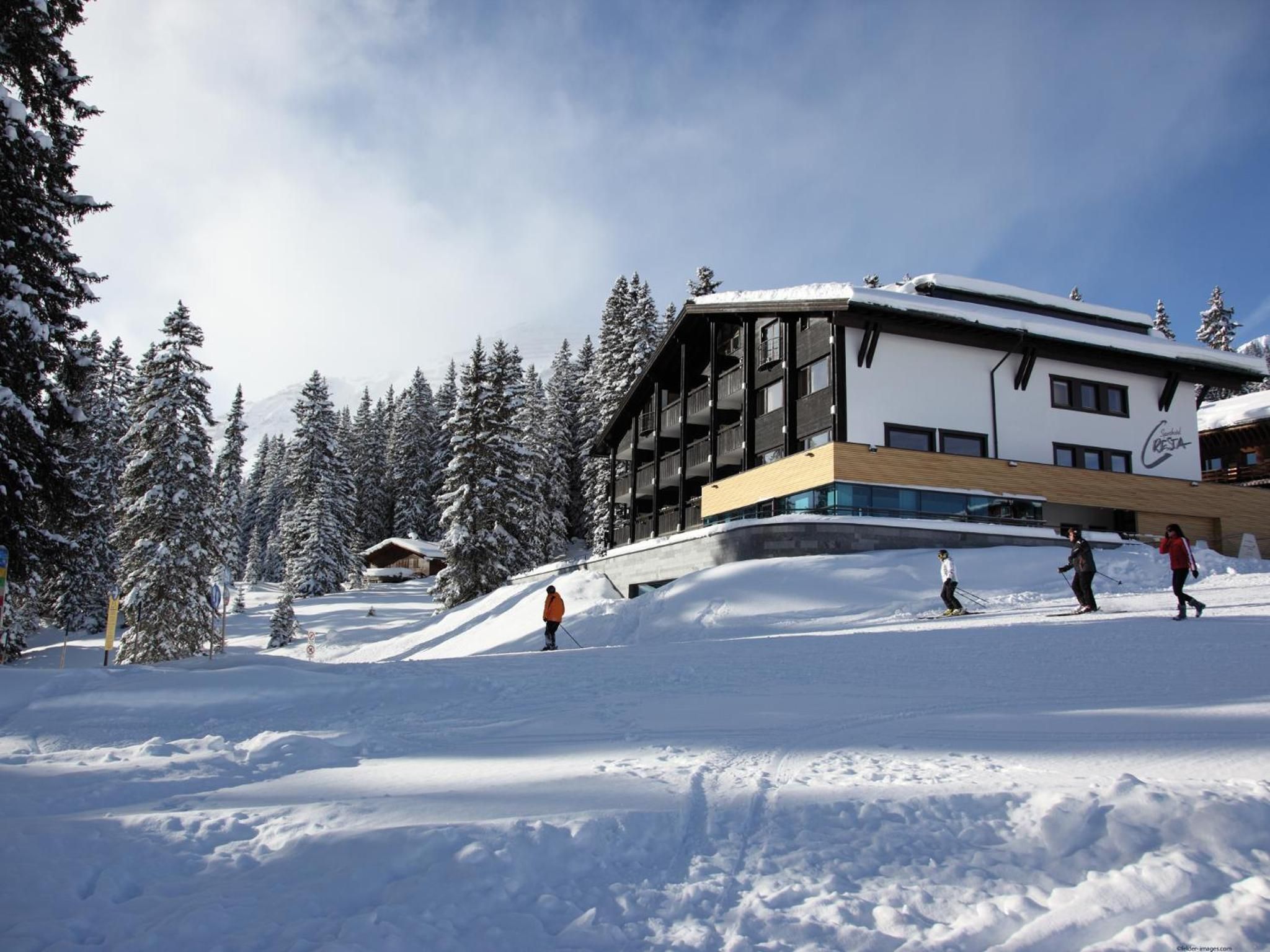Un centro de esquí con un edificio moderno, árboles cubiertos de nieve y esquiadores en las pistas.