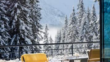 Área externa coberta de neve com mesa posta para dois, com vista para uma paisagem montanhosa.