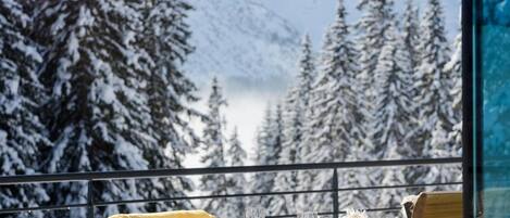 Un área de comedor al aire libre cubierta de nieve con una mesa lista para dos, con vista a un paisaje montañoso.