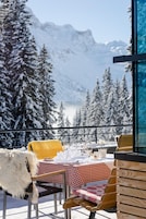 A snow-covered outdoor dining area with a table set for two, overlooking a mountainous landscape.