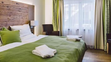 Ein Hotelzimmer mit einem großen Bett, einem Sessel, einem kleinen Tisch und einem Fenster mit Vorhängen.