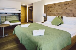 Habitación de hotel con una cama litera, una cama individual con ropa de cama verde, una mesita de noche y un cabecero de madera.