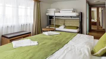 Ein Hotelzimmer mit Etagenbett, einem Einzelbett, einer Sitzbank, einem kleinen Tisch und einem Spiegel.